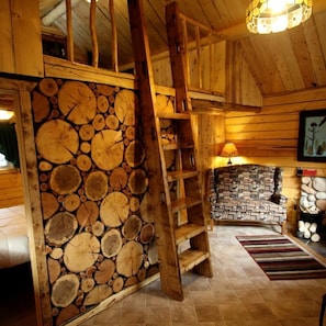 Un interior rústico con una pared de troncos de madera, una escalera, un tapete estampado y una chimenea.