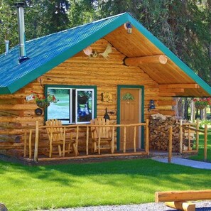 A log cabin with a green roof, wooden exterior, and a porch with chairs.