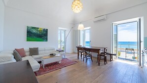 A spacious living room with a white sofa, a dining table, and a view of the ocean through large glass doors. - Ospedaletti by the Sea by Wonderful Italy (Ospedaletti)