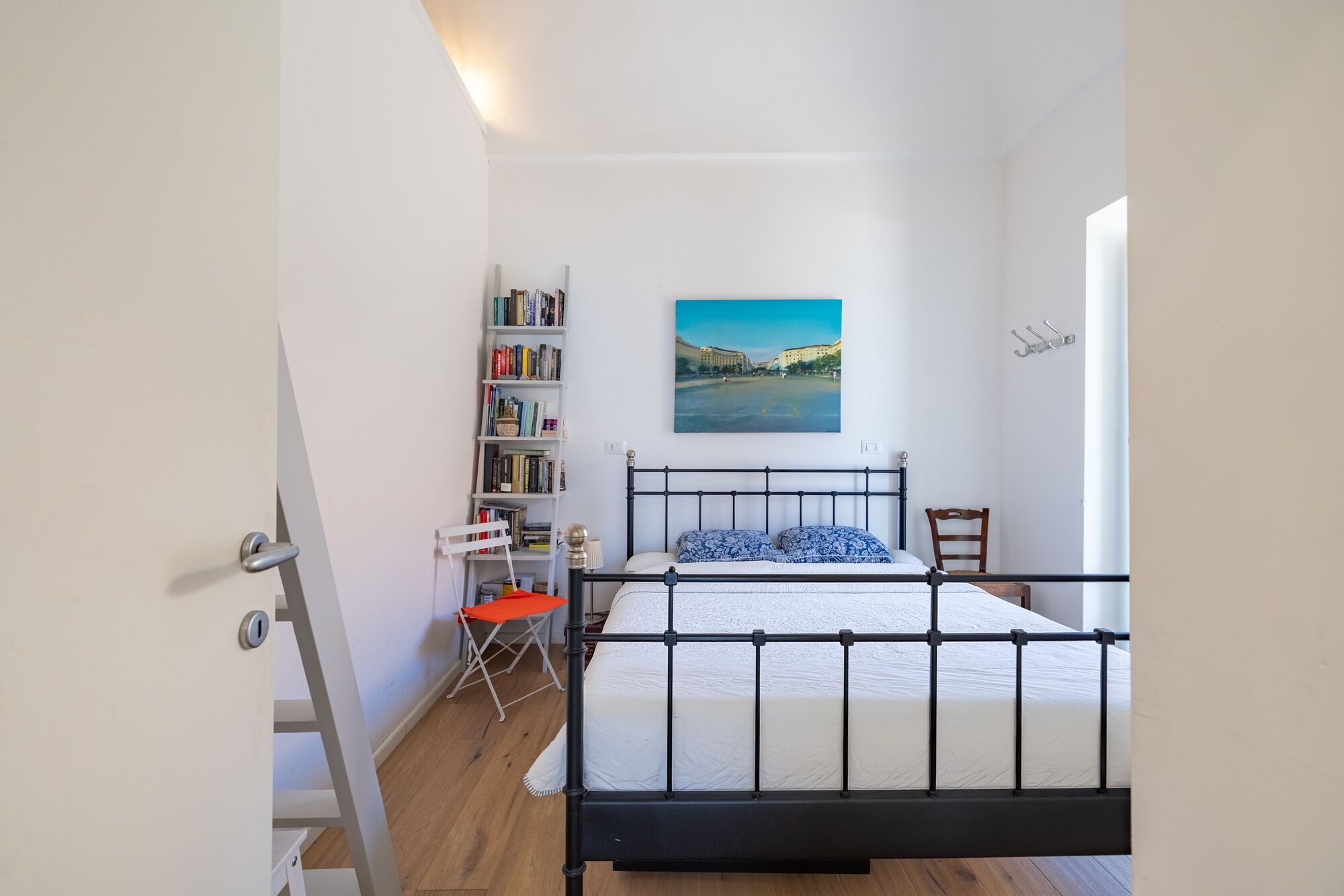 Ein Schlafzimmer mit einem Bett, einem Bücherregal, einem Sessel und einem Bild an der Wand.