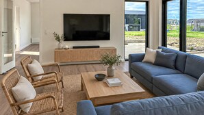 Ett modernt vardagsrum med en platt-TV, en soffa, ett soffbord och fåtöljer i rotting.