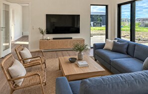 Ein modernes Wohnzimmer mit Flachbildfernseher, einer Couch, einem Couchtisch und Korbstühlen.