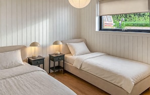 Ein Schlafzimmer mit zwei Betten, einem Fenster mit Blick auf Grünflächen und einem Nachttisch mit Lampe.
