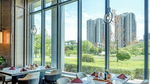 A modern dining area with large windows, tables set with red napkins, and a view of high-rise buildings. - Shaanxi Normal University International Education Building (Xi'an)