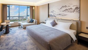 A hotel room with a large bed, a desk, a sofa, a small table, and a large window with a city view. - Shaanxi Normal University International Education Building (Xi'an)