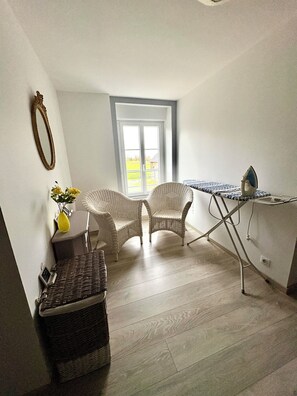 Una habitación con sillas de mimbre, una mesita con un florero, una cesta de mimbre y una plancha.
