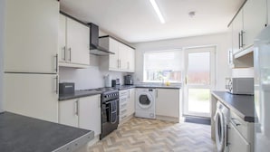 Une cuisine moderne avec des meubles blancs, un four encastré, un lave-linge et un réfrigérateur.