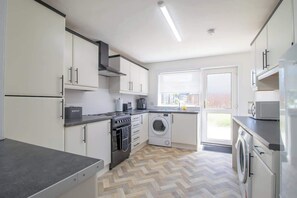 Une cuisine moderne avec des meubles blancs, un four encastré, un lave-linge et un réfrigérateur.