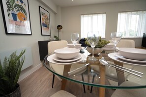 A dining area with a glass table, white plates, and clear glassware. - Church House by Guestz (Filton)