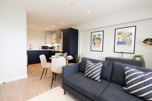 A modern living room with a dark grey sofa, a dining table, and a kitchen in the background. - Church House by Guestz (Filton)