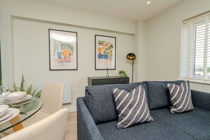 A modern living room with a grey sofa, a glass dining table, and two framed artworks on the wall. - Church House by Guestz (Filton)