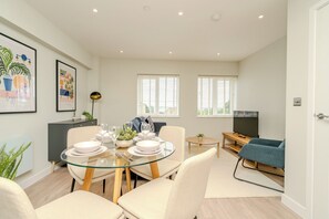 Un salon moderne avec une table à manger en verre, des sièges confortables, un téléviseur à écran plat et des œuvres d’art accrochées aux murs.