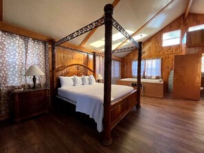 Una cama con dosel en una habitación de madera con suelo de madera, una mesita de noche con lámpara y una ventana con cortinas.