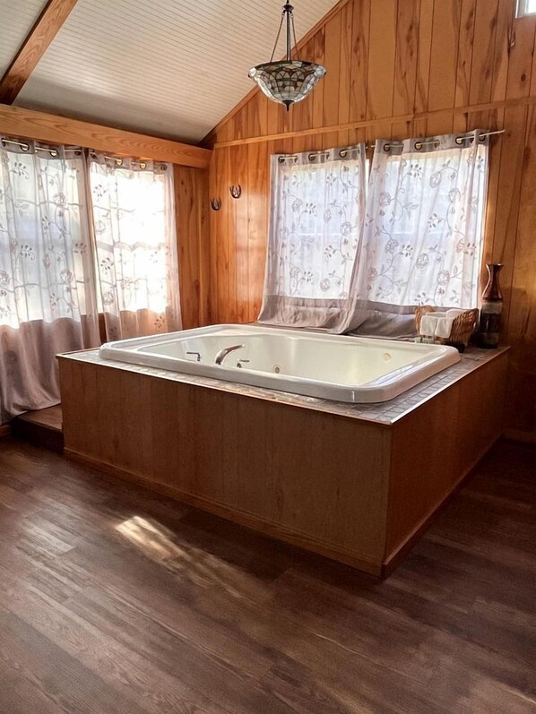 A wooden cabin interior with a large bathtub, wooden walls, and a hanging light fixture.