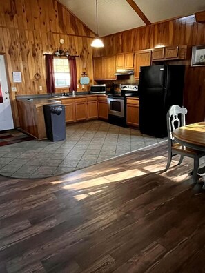 Una cocina con armarios de madera, un refrigerador negro, una estufa y una mesa de comedor con sillas.