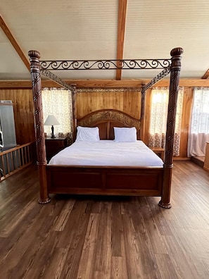 Una cama con dosel y tablero de madera, suelo de madera y una ventana con cortinas.