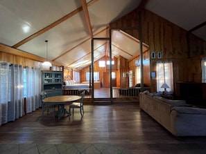 Una habitación amplia con techo de madera, una mesa de comedor con sillas, un sofá y una televisión.