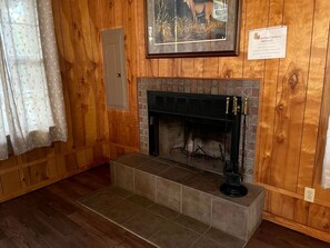 A fireplace with a tiled surround, wooden walls, a framed picture above it, and a sign with instructions.