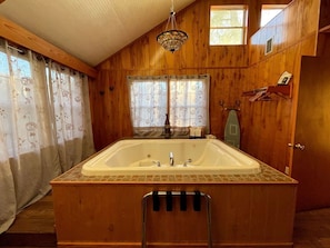 Une salle de bain rustique, avec des murs en bois, une grande baignoire, un luminaire suspendu et une fenêtre agrémentée de rideaux.