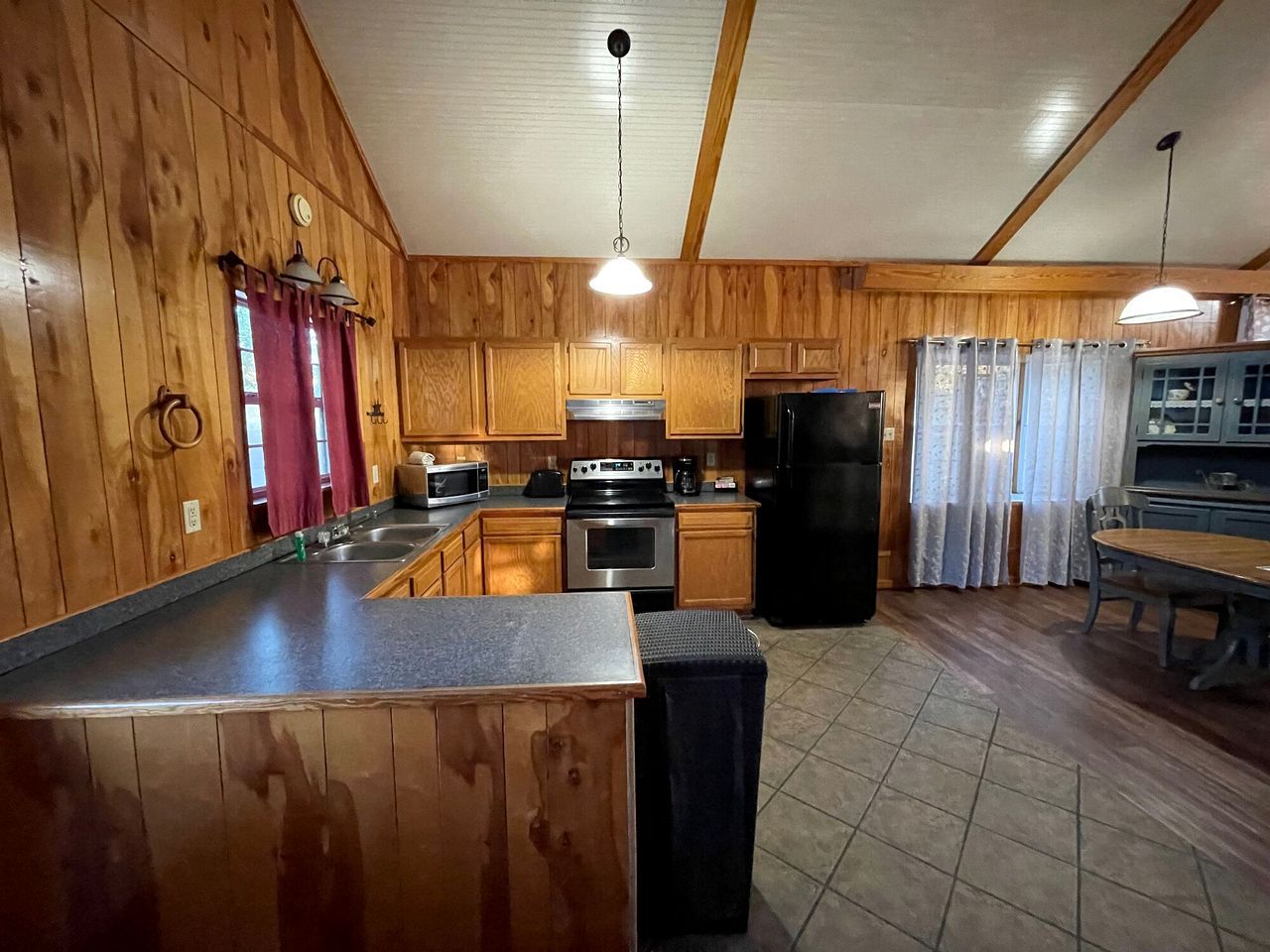 A kitchen with wooden walls, a central island, stainless steel appliances, and a dining area with a table and chairs.