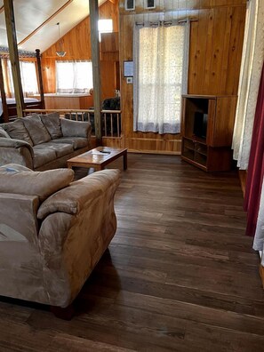 Un salón con suelo de madera, un conjunto de sofás, una mesa de centro y un mueble para televisión.
