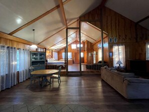Una habitación amplia con techo de madera, una mesa de comedor con sillas, un sofá y una televisión.