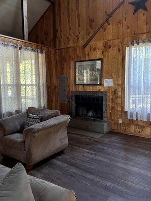 Ein Zimmer mit Holzwänden, einem Kamin, einer Couch und Vorhängen.