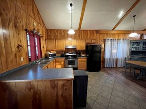 A kitchen with wooden walls, a central island, stainless steel appliances, and a dining area with a table and chairs.