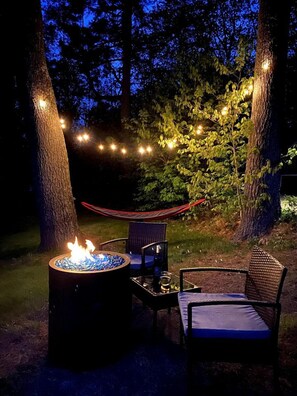A nighttime outdoor seating area with a fire pit, two chairs, and string lights. - Cabin 4 (Lincolnville)