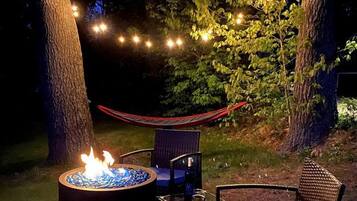 A nighttime outdoor seating area with a fire pit, two chairs, and string lights.