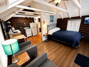 A cozy cabin interior with a bed, seating area, kitchenette, and a TV. - Cabin 4 (Lincolnville)