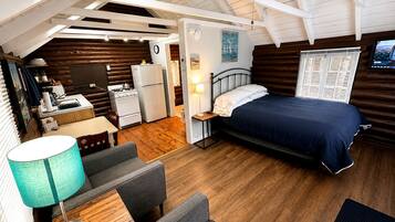 Un interior de cabaña acogedor con una cama, zona de estar, kitchenette y un televisor.