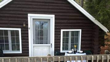 A log cabin with a porch, a door, and two windows.