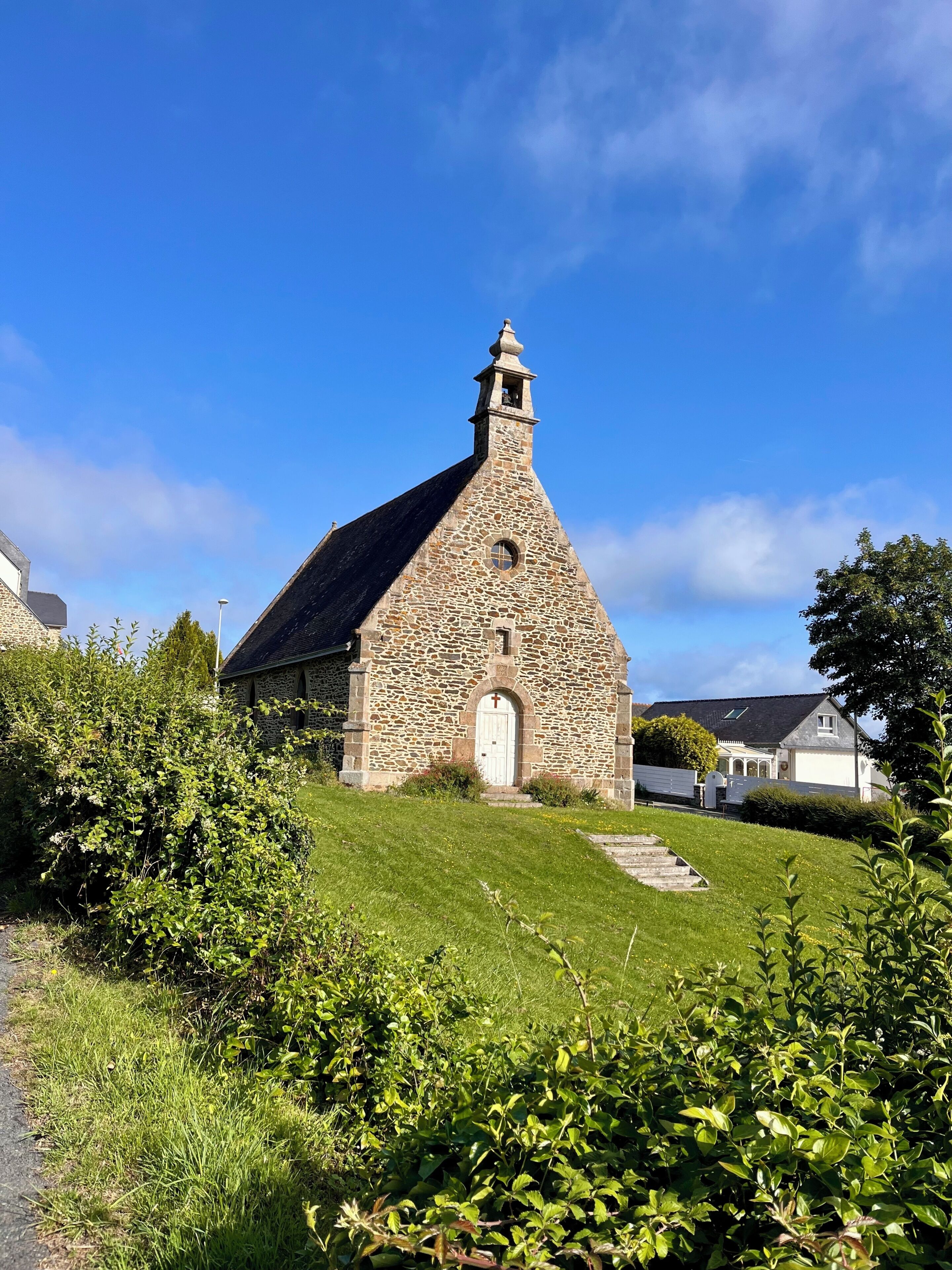 Eine steinerne Kirche mit Glockenturm, umgeben von viel Grün und blauem Himmel.