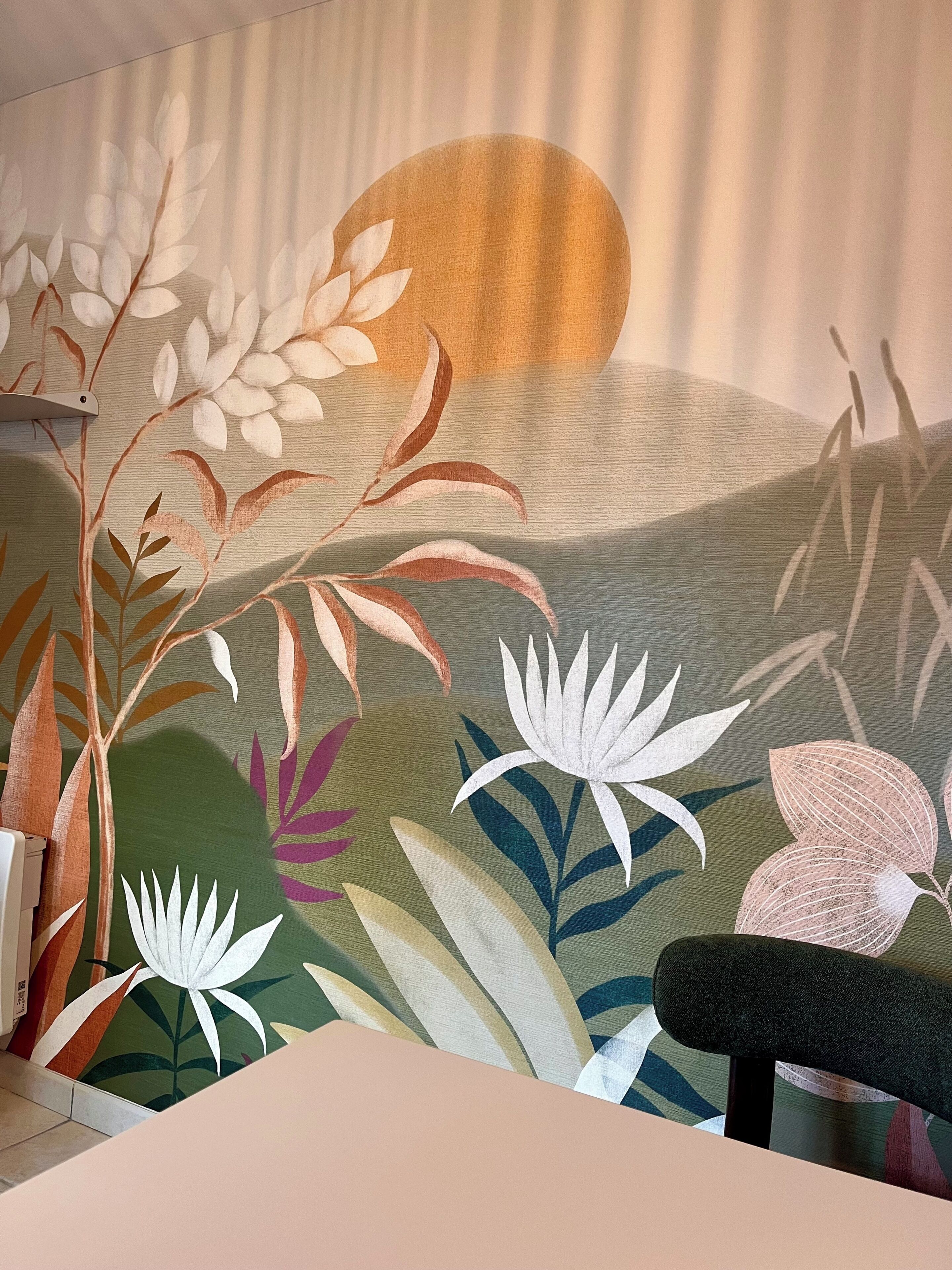 Een kamer met een muurschildering van gestileerde planten en een grote zon.