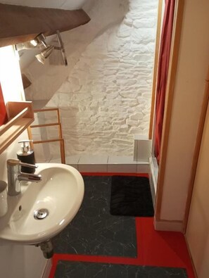 Un baño con un lavabo blanco, una silla de madera, un tapete rojo y una pared de piedra.