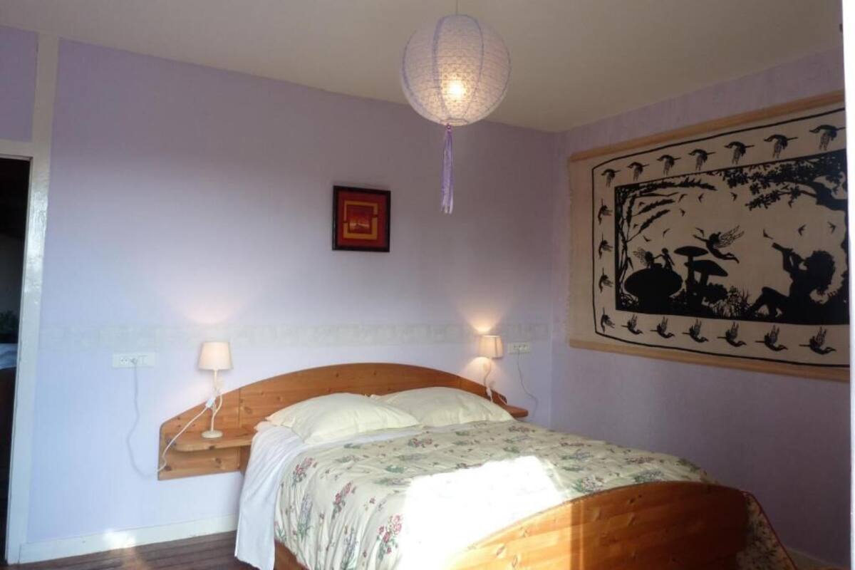 A bedroom with a wooden bed, two bedside lamps, a hanging light fixture, and a wall painting.