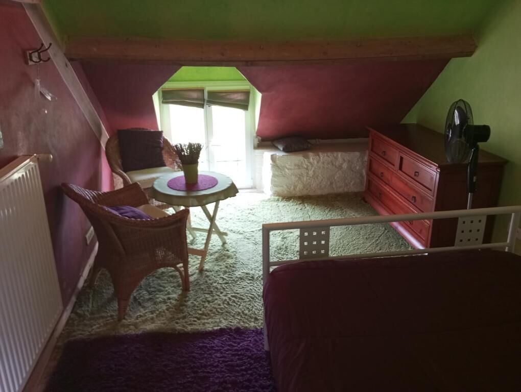A small, cozy attic bedroom with a bed, a dresser, a chair, a table, and a window.
