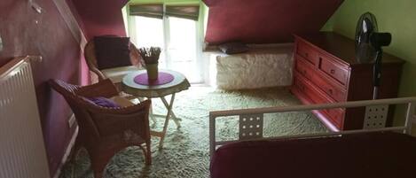Un dormitorio acogedor en el ático, con cama, cómoda, silla, mesa y ventana.
