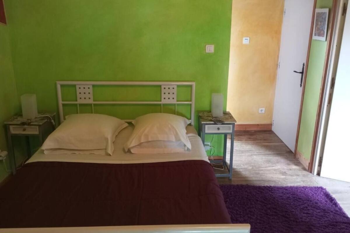 A room with a bed, bedside tables, a nightstand, and a door leading to another room.
