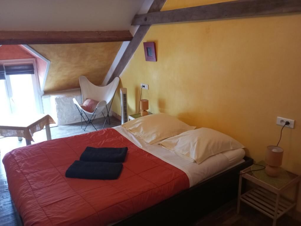 A bedroom with a bed, a chair, a bedside table, and a window.
