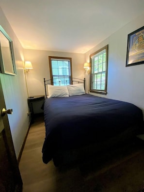 Quarto com cama, duas luminárias de cabeceira, uma janela e um quadro na parede.