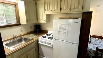A compact kitchen with a sink, stove, and refrigerator, wooden flooring, and light-colored cabinets.