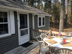 Uma cabana pequena com varanda, uma mesa e cadeiras, e uma janela.