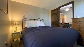 Een slaapkamer met een bed, nachtkastje, lamp, kaptafel en een deur naar een andere kamer.