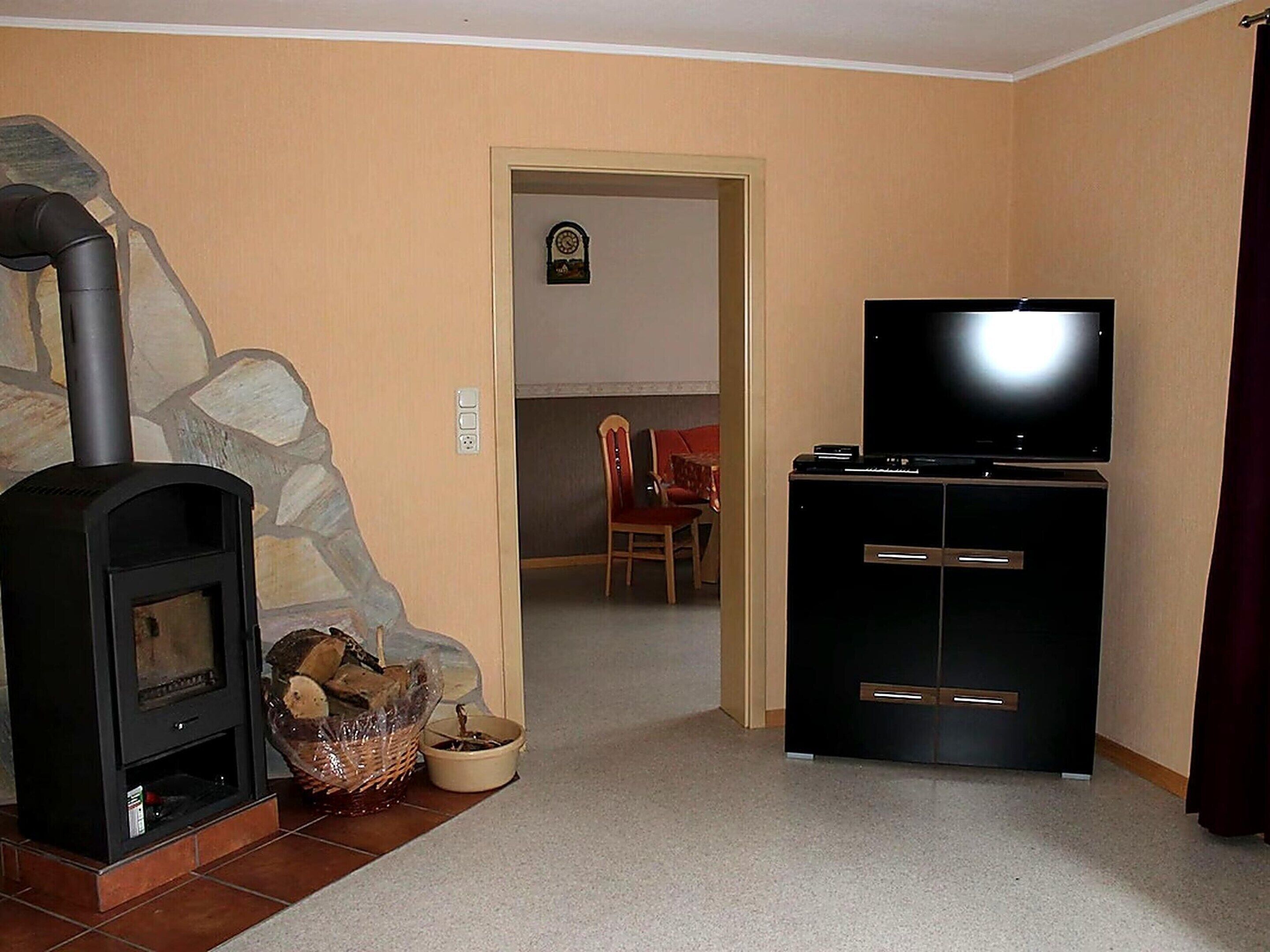 Una sala de estar con chimenea, un televisor sobre un mueble bajo y un comedor al fondo.