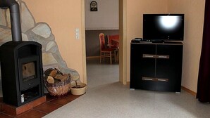 Un salon avec une cheminée, un téléviseur posé sur un meuble et un coin repas à l’arrière-plan.