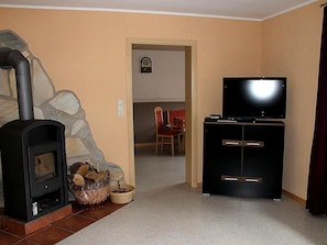 Ein Wohnzimmer mit Kamin, einem Fernseher auf einem Schrank und einem Essbereich im Hintergrund.