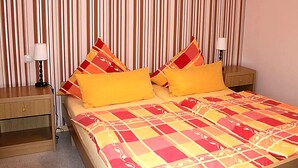 Habitació d'hotel amb paper pintat a ratlles, un llit amb colcha de quadres, dues taules de nit amb làmpades i una tauleta de nit.