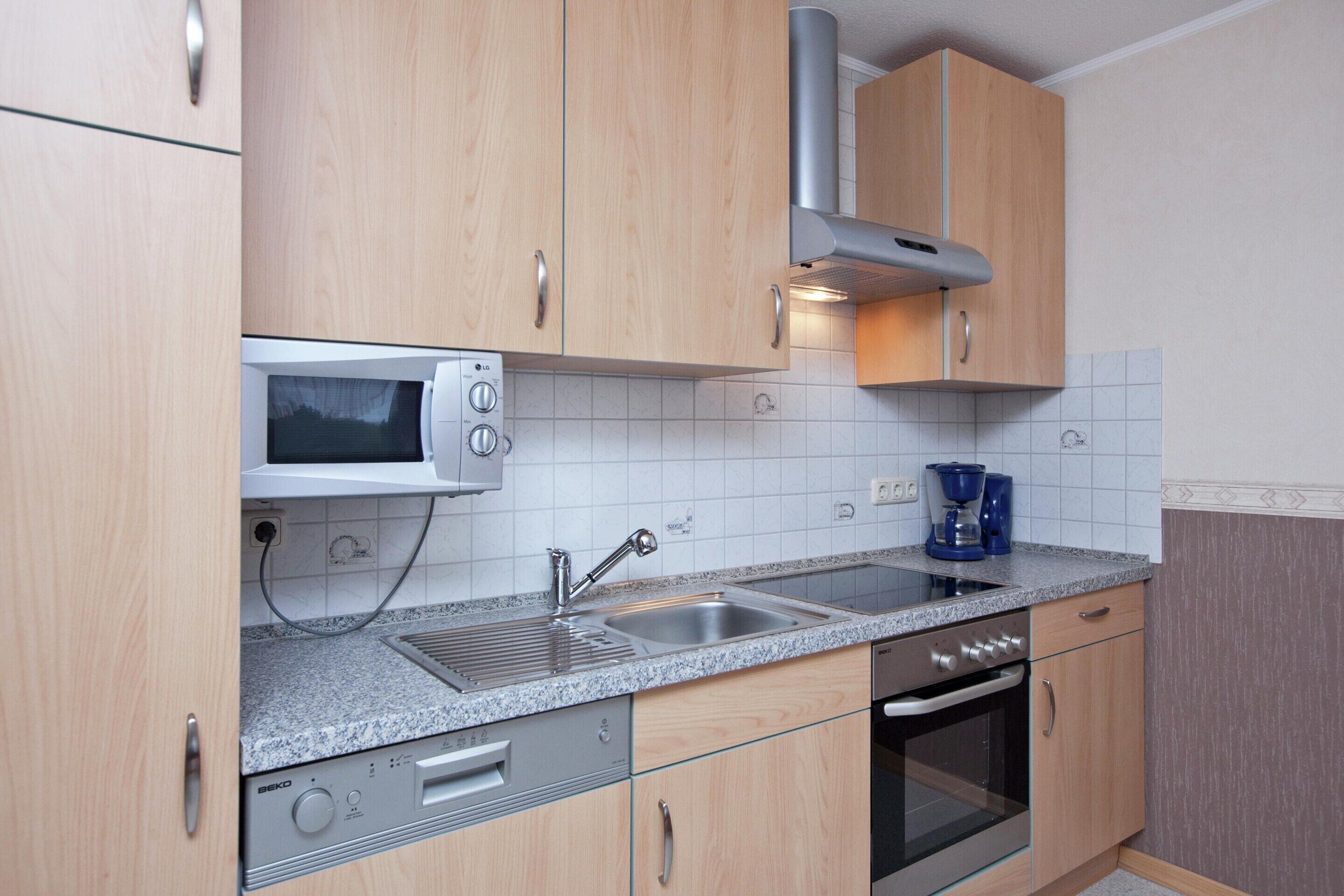 Eine Küche mit Holzausstattung, einer Mikrowelle, einem Spülbecken, einer Kaffeemaschine und einem Backofen.
